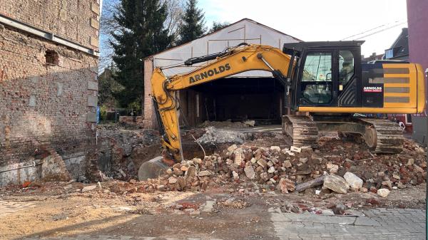 Ein Bagger bricht Steine vor der kalten Halle auf.