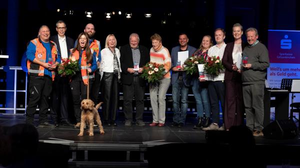 Foto von 12 Personen und einem Hund auf einer Bühne, die den Ehrenamtspreis erhalten haben.